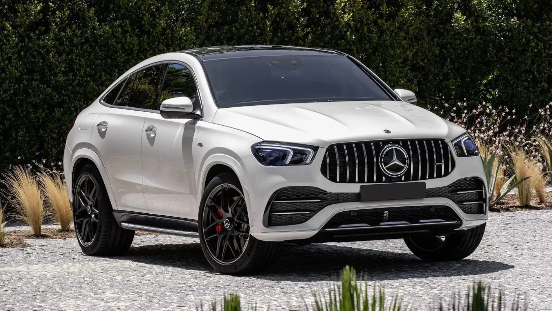 A white mercedes gle coupe parked in front of some bushes.